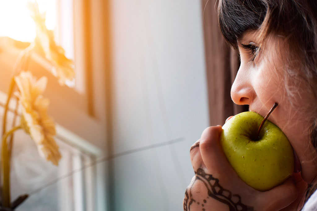 niña mirando por la venta queriendo comer rápido una manzana verde