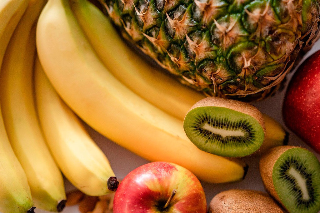 frutas encima de una mesa de madera kiwi por la mitad, piña, banana, manzana