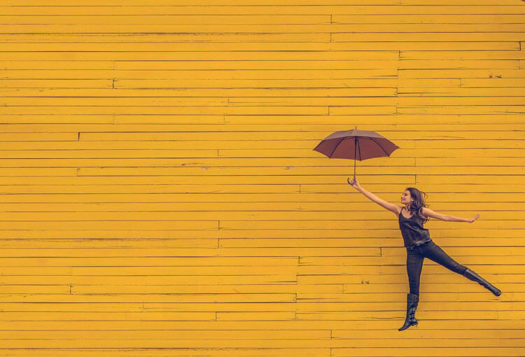 mujer feliz sosteniendo un paragua delante de un fondo amarillo