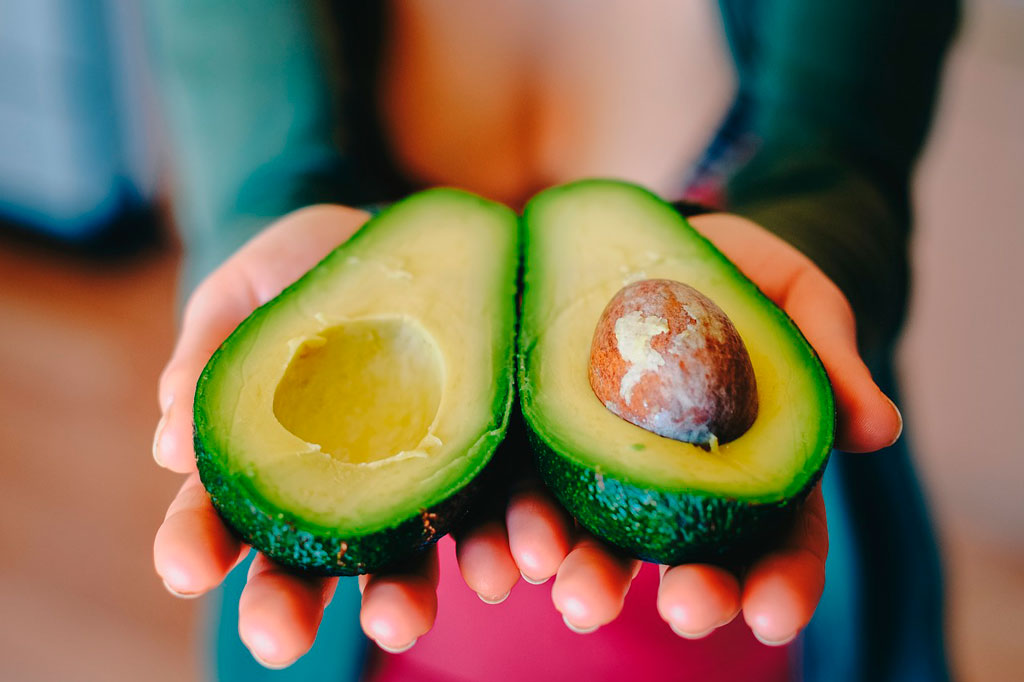 mujer sosteniendo aguacate frescos picado por la mitad